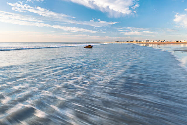 A rippled wave rolls in reflecting the sky above at Hampton Beach in Hampton, NH